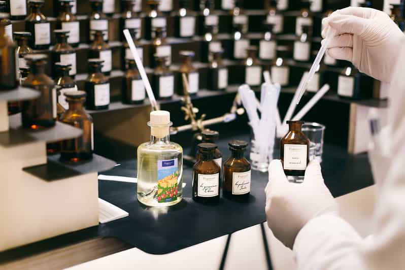 Un artisan parfumeur manipulant des flacons d'essences et utilisant une pipette pour mélanger des concentrés de parfum dans un atelier de création. La scène met en valeur les outils et les matières premières utilisés dans la fabrication de parfums.