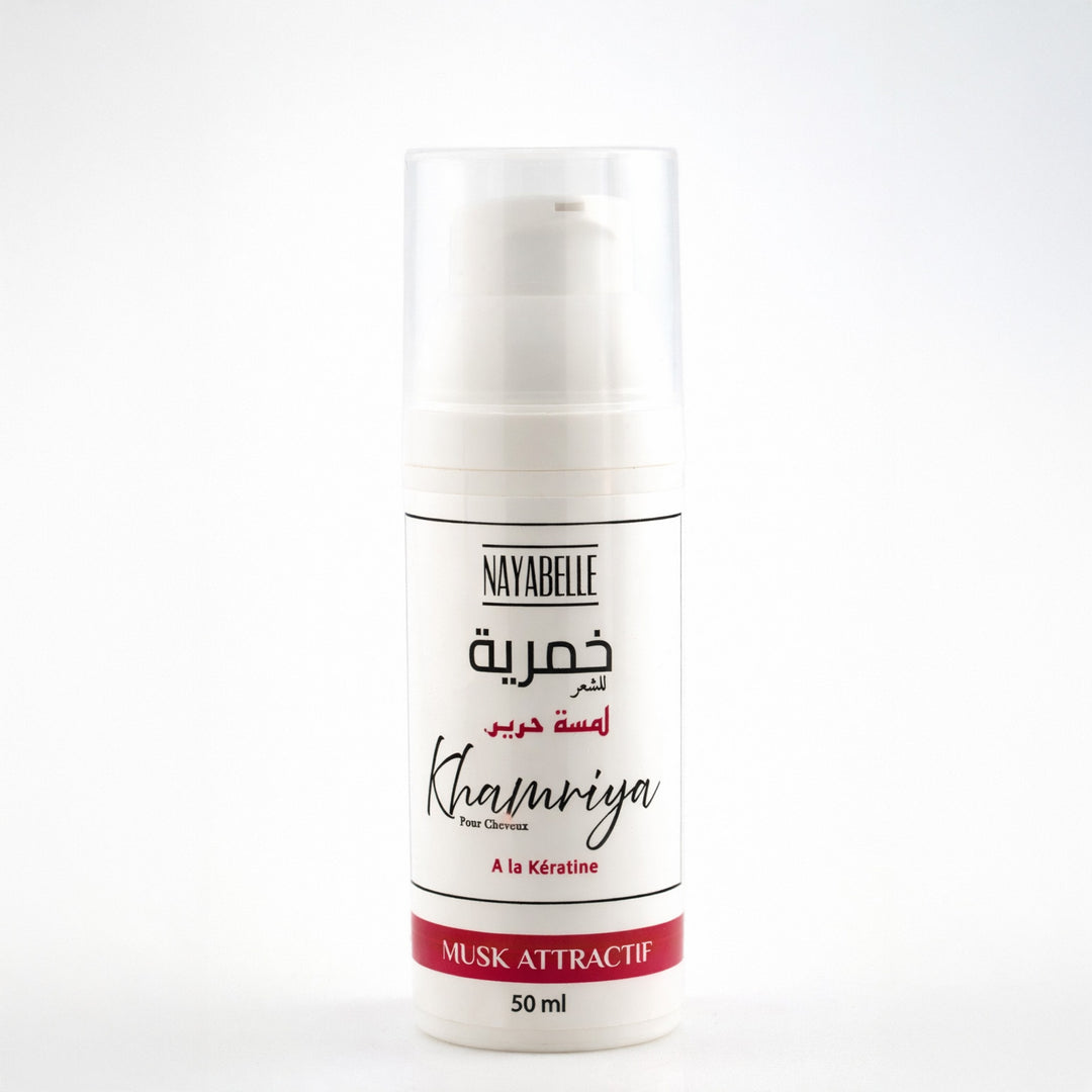 Flacon pompe blanc élégant de Khmariya pour cheveux de la marque Nayabelle, gamme Lamesat Harir (Touche de Soie). L'étiquette épurée précise une formulation enrichie à la Kératine pour apporter douceur et brillance intense à la chevelure. Ce parfum capillaire au Musk Attractif est conçu pour offrir une tenue longue durée et une expérience sensorielle unique tout en garantissant une utilisation sécurisée pour la fibre capillaire.