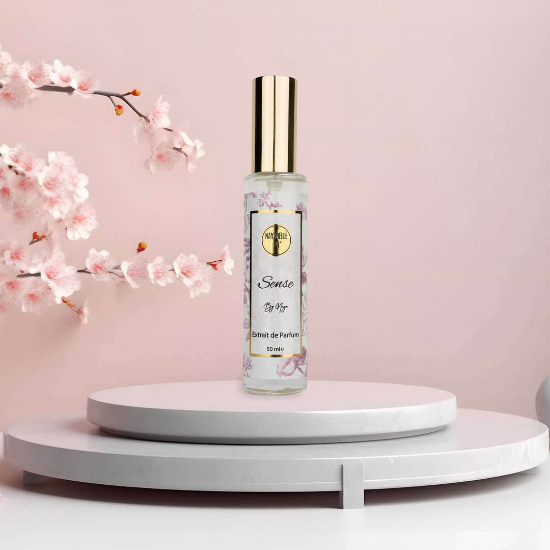 Flacon de 50 ml du parfum Sense de Nayabelle, posé sur un podium circulaire blanc avec un décor de fleurs de cerisier et un fond rose pastel.