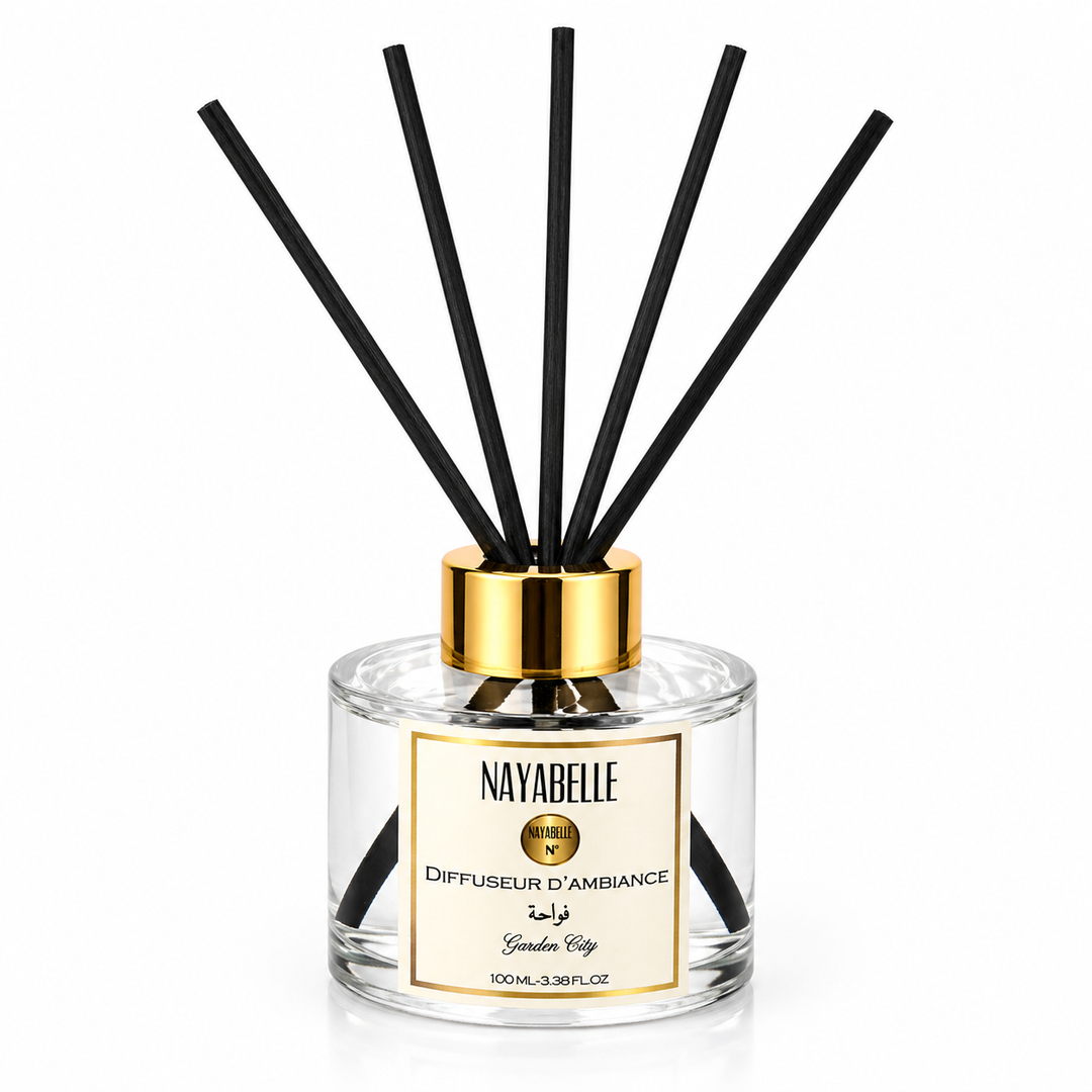 Diffuseur d'ambiance Nayabelle 'Garden City' de 100 ml, avec flacon en verre transparent et tiges noires pour une diffusion élégante et continue du parfum. Le bouchon doré ajoute une touche de luxe pour parfumer délicatement votre intérieur. 