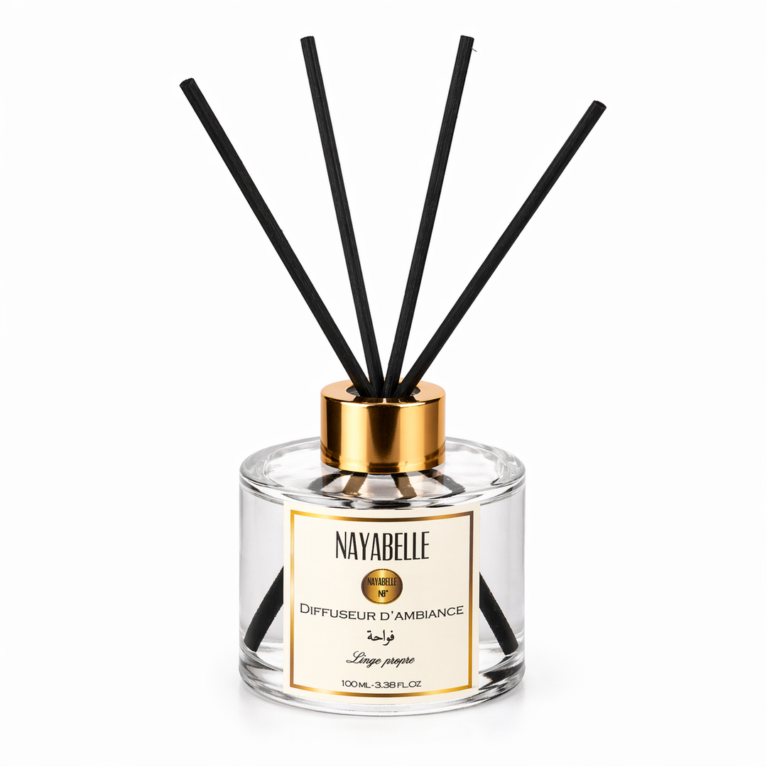 Diffuseur d'ambiance Nayabelle 'Linge Propre' de 100 ml, avec un flacon en verre transparent, des tiges noires et un bouchon doré. Parfum délicat pour une atmosphère fraîche et apaisante dans votre intérieur