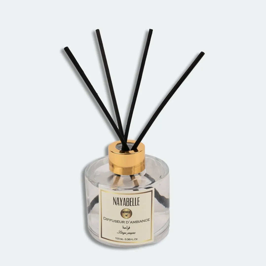 Diffuseur d'ambiance Nayabelle 'Linge Propre' de 100 ml, avec un flacon en verre transparent, des tiges noires et un bouchon doré. Parfum délicat pour une atmosphère fraîche et apaisante dans votre intérieur