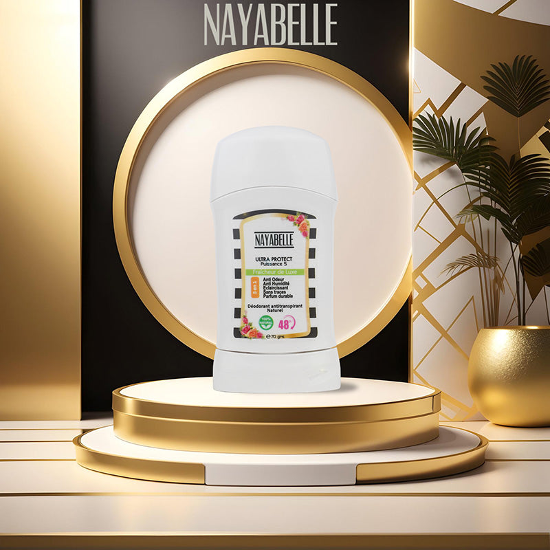 Déodorant stick Nayabelle Ultra Protect posé sur un podium doré élégant, avec un fond noir et or raffiné portant le logo Nayabelle en haut. Décor luxueux avec des motifs géométriques dorés et un vase contenant des plantes vertes.