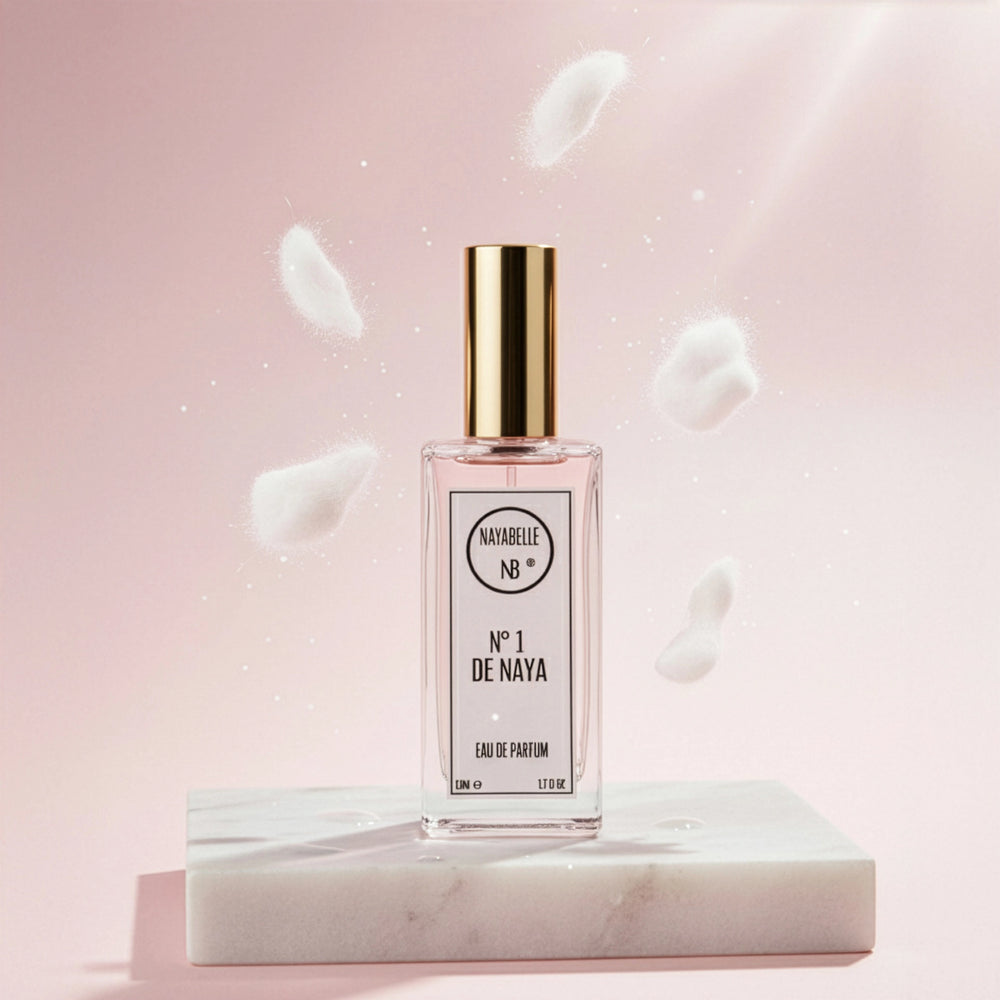 Parfum N° 1 de Naya par Nayabelle. Flacon posé sur un socle de marbre blanc, entouré d'éléments blancs et cotonneux flottant dans les airs, symbolisant le musc blanc et la pureté. Photo créative pour e-commerce.