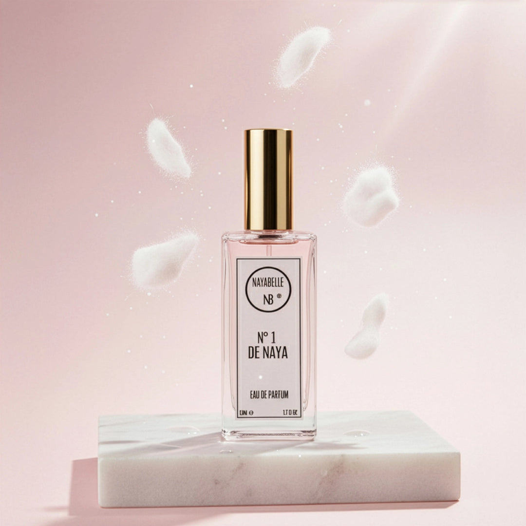 Parfum N° 1 de Naya par Nayabelle. Flacon posé sur un socle de marbre blanc, entouré d'éléments blancs et cotonneux flottant dans les airs, symbolisant le musc blanc et la pureté. Photo créative pour e-commerce.