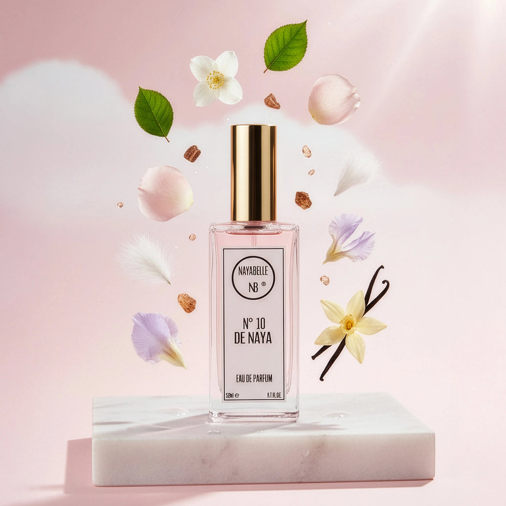Parfum N° 10 de Naya par Nayabelle. Flacon posé sur un socle de marbre blanc, entouré des ingrédients de la fragrance flottant dans les airs : vanille, fleurs blanches, pétales et feuilles vertes. Photo créative pour e-commerce.