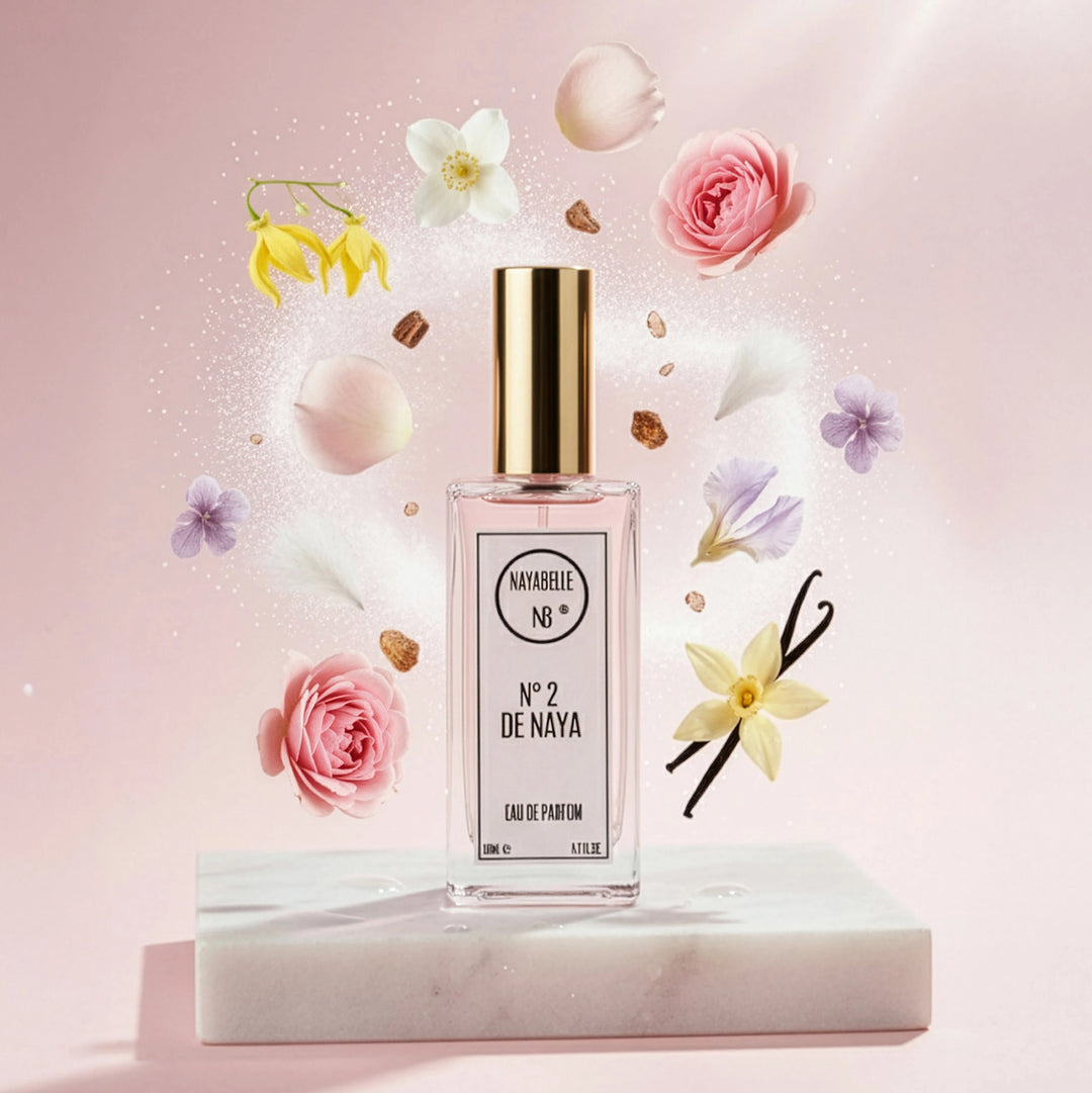Parfum N° 2 de Naya par Nayabelle. Flacon posé sur un socle de marbre blanc, entouré des ingrédients de la fragrance flottant dans les airs : roses, pétales, vanille et fleurs blanches. Photo créative pour e-commerce.
