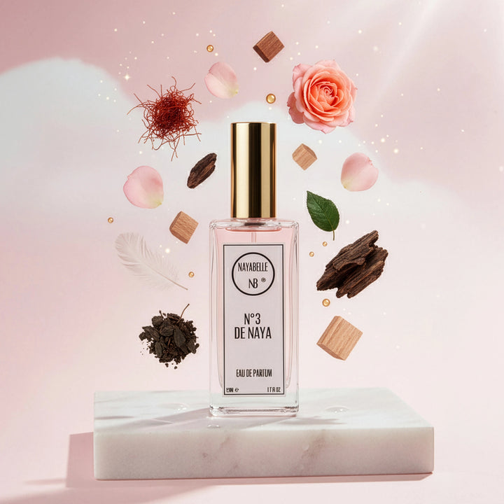 Parfum N° 3 de Naya par Nayabelle. Flacon posé sur un socle de marbre blanc, entouré des ingrédients de la fragrance flottant dans les airs : safran, rose, copeaux et morceaux de bois sombre. Photo créative pour e-commerce.