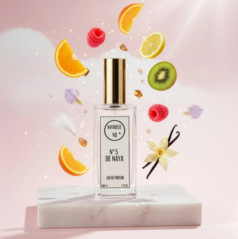 Parfum N° 5 de Naya par Nayabelle. Flacon posé sur un socle de marbre blanc, entouré des ingrédients de la fragrance flottant dans les airs : orange, citron, kiwi, framboises et gousses de vanille. Photo créative pour e-commerce.