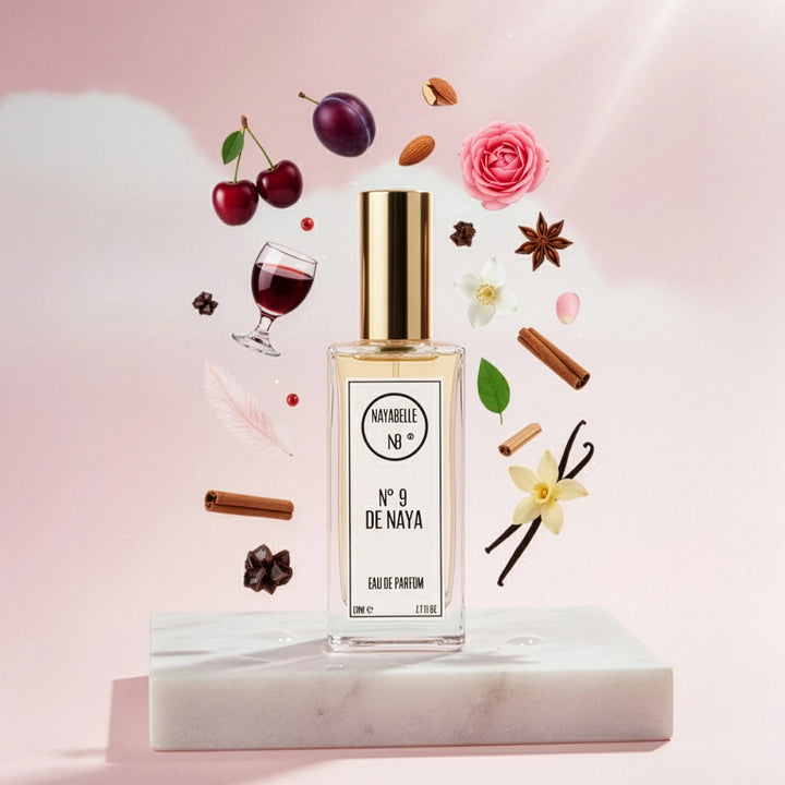 Parfum N° 9 de Naya par Nayabelle. Flacon posé sur un socle de marbre blanc, entouré des ingrédients de la fragrance flottant dans les airs : cerise, prune, amande, cannelle, vanille et épices. Photo créative pour e-commerce.